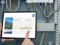 Ein Tablet mit Energieverbrauchsdaten und Zertifizierungslogo wird von einer Person vor ein elektrisches Gerät gehalten.