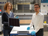 Projektleiterin Dr. Laura Stevens zeigt eines der III-V-Germanium-PV-Module mit einer Rekordeffizienz von 34,2 Prozent. Leonhard Böck ist Projektmitarbeiter und hat maßgeblich am – vor ihm liegenden – III-V-Silizium-PV-Modul mit 31,3 Prozent Effizienz mitgearbeitet.