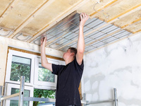 Ein Mann bringt eine Flächenheizung aus Altpapier an einer Decke an.